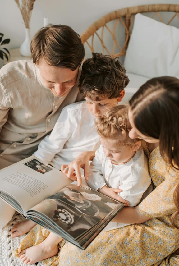 A family of four is reading a book together on a bed.