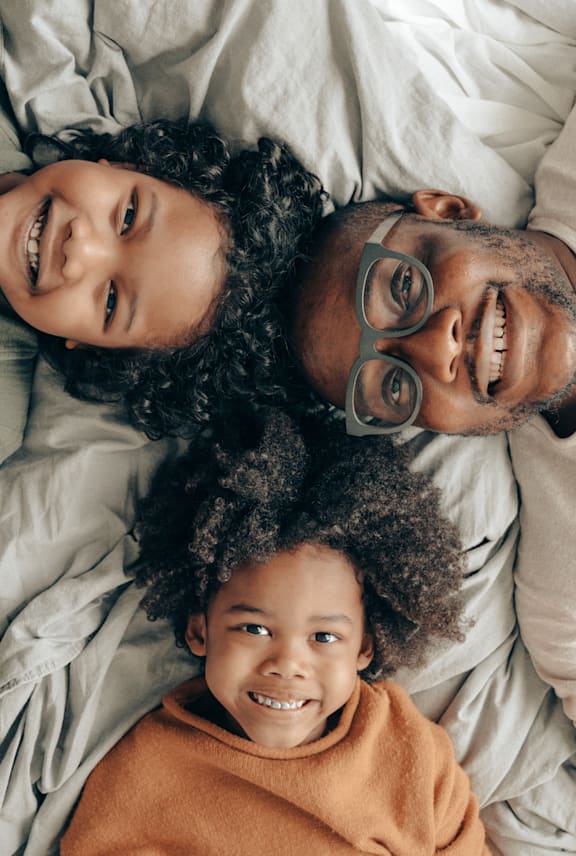 A man and two children are lying down together on a bed. at Mountain Terrace Apartments , Westminster, 80031
