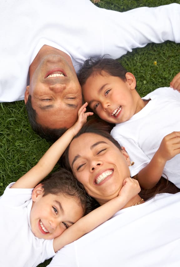 A family of three is lying on the grass and smiling. at Meeker Commons Apartments , Greeley