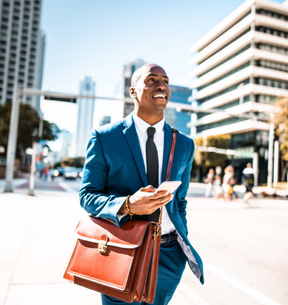 a man in a blue suit and tie holding a brown leather briefcase walking down the street