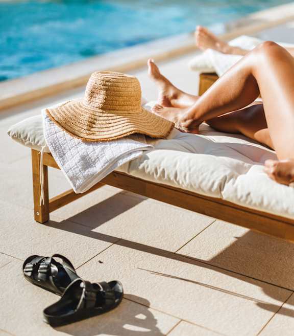 A woman in a straw hat lounges by a pool.