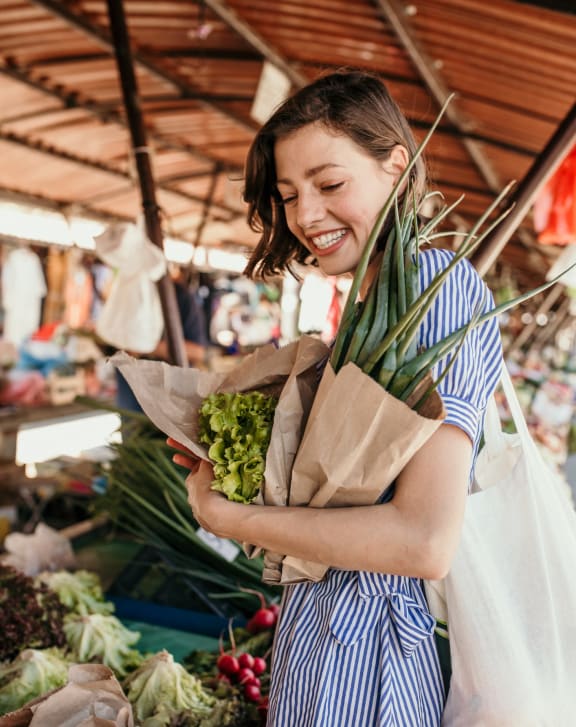 a woman holding a bag of vegetables at a market