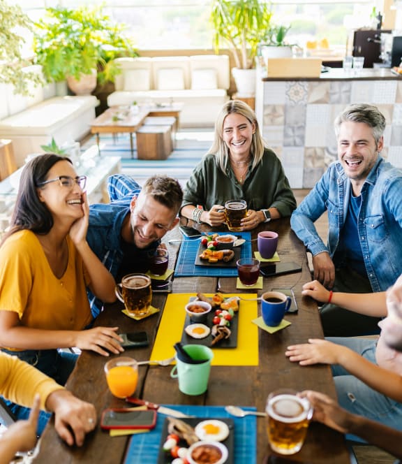 a group of people sitting around a table eating food and drinking beer