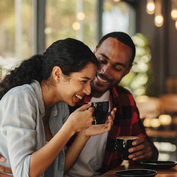 A man and a woman are sitting at a table, sharing a drink and a moment of laughter.