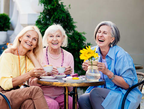 Three women are sitting at a table outside, laughing and enjoying each other's company.