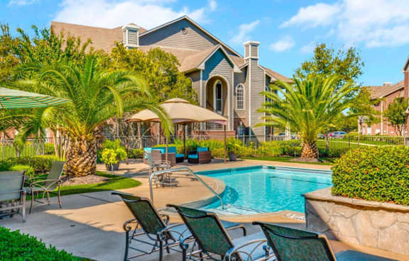 a swimming pool with chairs and umbrellas in front of a house