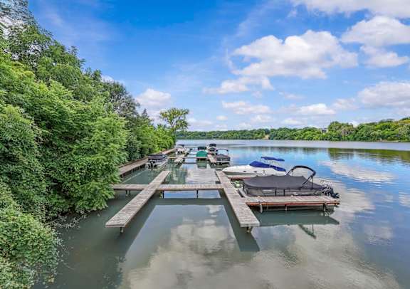 A dock with a boat and chairs on a lake surrounded by trees.