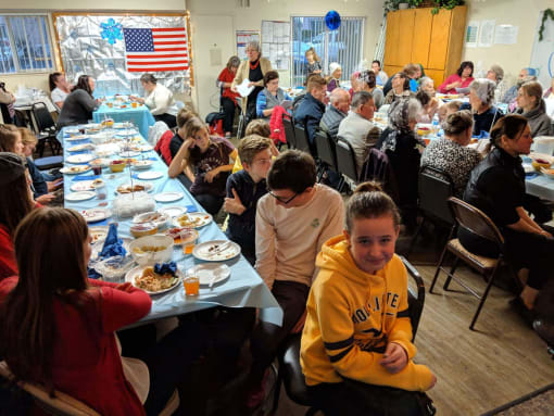 Resident families share a meal at long tables in a community room
