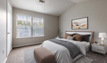 A bedroom with a large bed, a nightstand, and a window with blinds.