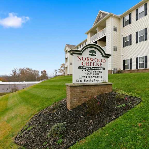 A sign for Norwood Greene stands in front of a white building.