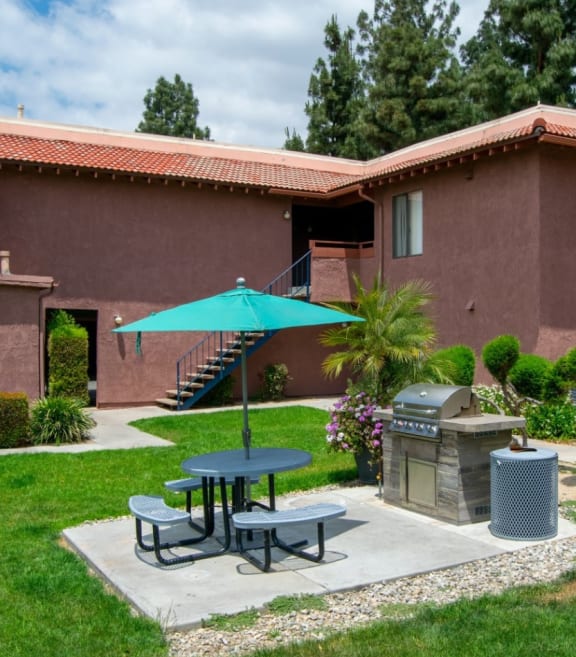 a patio with a table and umbrella in front of a building at Summer Meadows in Riverside, CA