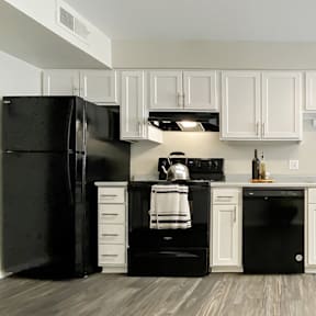 A black refrigerator and oven in a kitchen with white cabinets.