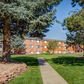 A building is behind a grassy area with trees and a stone wall.
