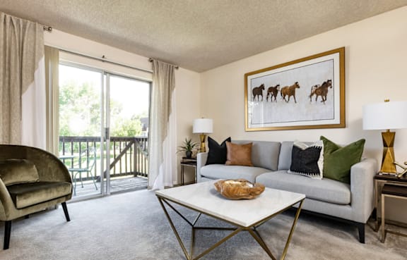 A living room with a grey couch, a green chair, and a painting of horses on the wall.