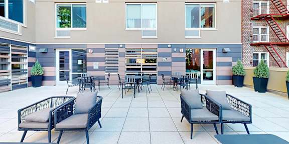 A patio with chairs and a table is surrounded by apartment buildings.