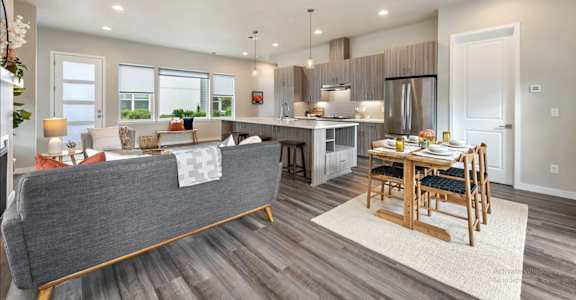 A modern living room with a grey sofa and a wooden dining table set for two.