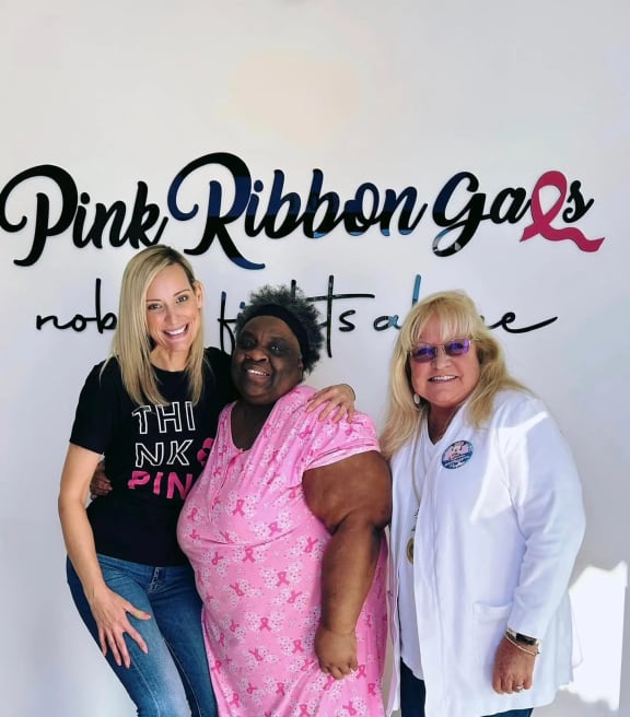 three women posing for a photo in front of a pink ribbon gala sign