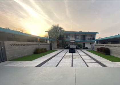 A sunset view of a driveway leading to a house with a palm tree in the background.