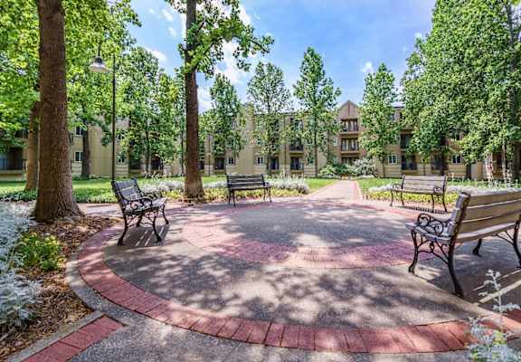 A circular brick patio with benches is surrounded by trees.