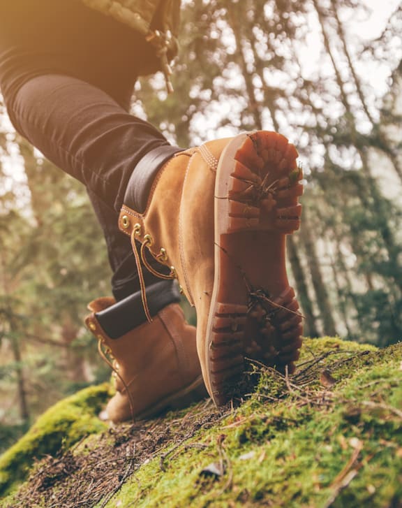 A person wearing brown boots standing on a mossy rock in a forest. at The Dean at Creekview Apartments, Newark, Delaware