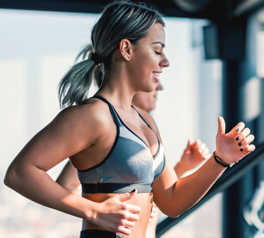 A woman in a grey sports bra and leggings is running on a treadmill.