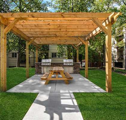 A wooden pavilion with a picnic table in the middle of a grassy area.