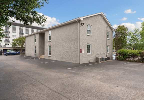 A grey building with a parking lot in front.
