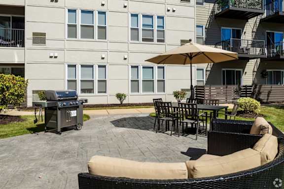 a patio with a grill and tables in front of an apartment building