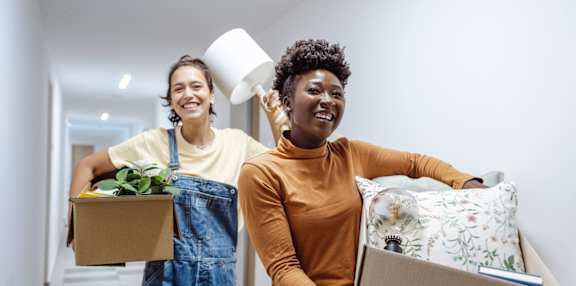 Two women carrying boxes with items inside, one holding a lamp.
