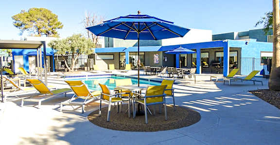 A blue umbrella is in the middle of a table and chairs.