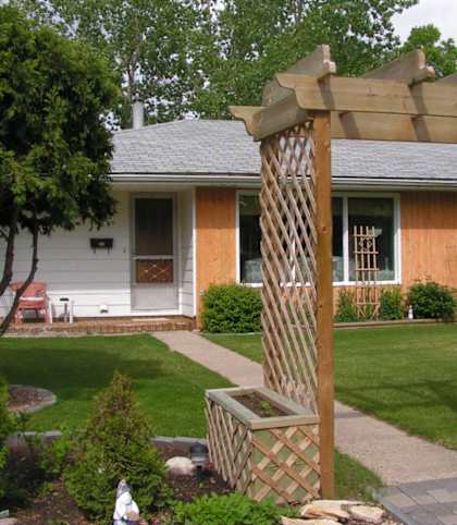 a yard with a wooden arbor in front of a house