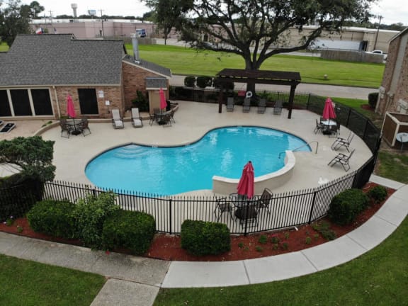 an above ground pool with a fence around it and a patio with chairs and umbrellas