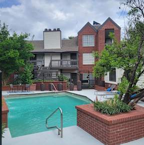 A pool surrounded by a brick wall and a tree.