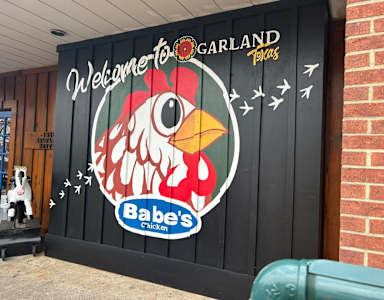 A mural of a chicken with the text "Welcome to Garland" and "Babe's Chicken" on a black wall.
