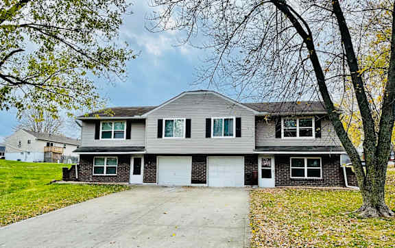 A two-story house with a garage is surrounded by a driveway and trees.
