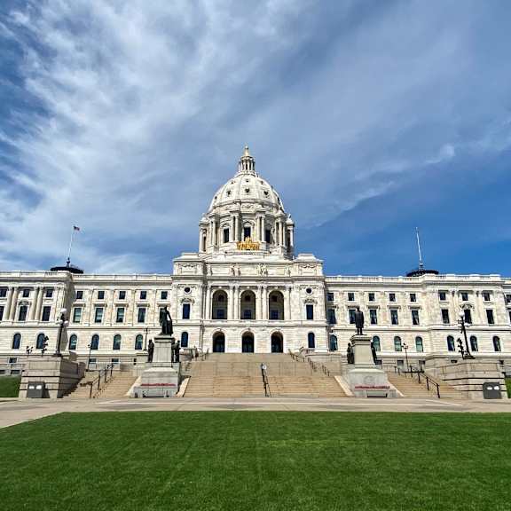 A large, white, neoclassical building with a dome on top and a statue in front.