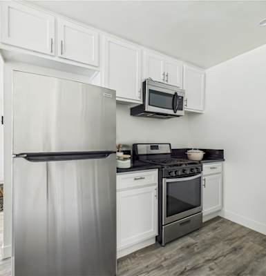 A modern kitchen with a refrigerator, microwave, oven, and a chair.
