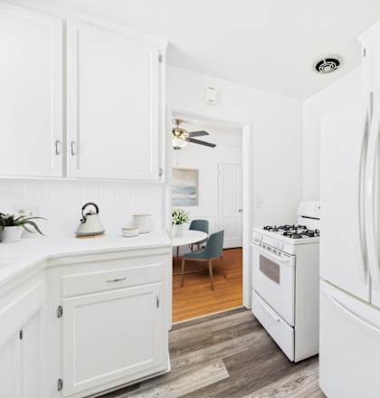 A white LG refrigerator stands in a kitchen with white cabinets and a wooden floor.