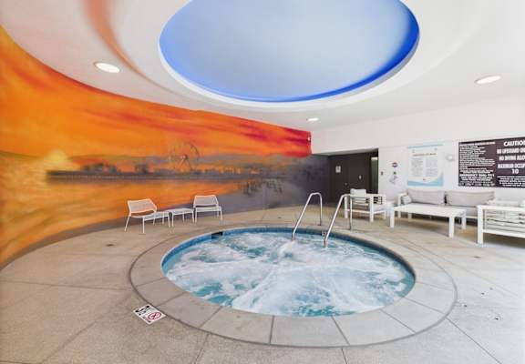 A hot tub in a room with a sunset mural on the wall.