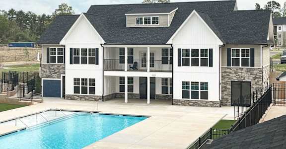 A large white house with a black roof and a pool in front.