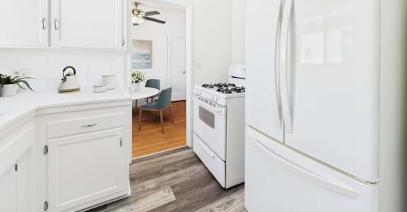 A white LG refrigerator stands in a kitchen with white cabinets and a wooden floor.