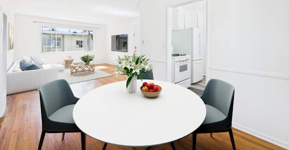 A white dining table with a bowl of fruit on it and two chairs.