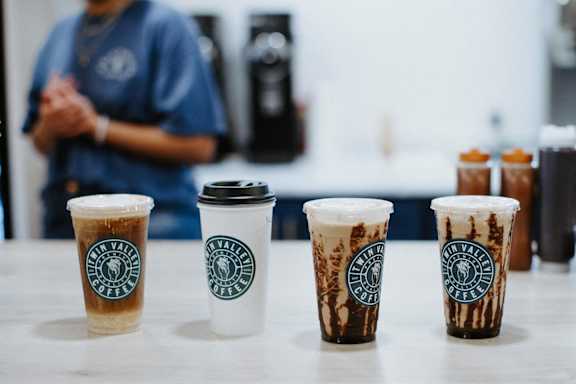 four cups of starbucks coffee on a table with a person in the background