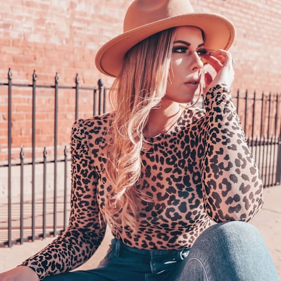 A woman in a leopard print top and blue jeans is sitting on the ground.