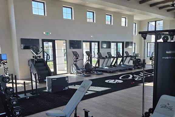 A gym with a variety of equipment including weights, treadmills, and a bench press. at Stella Luxury Apartment Homes in San Tan Valley, AZ