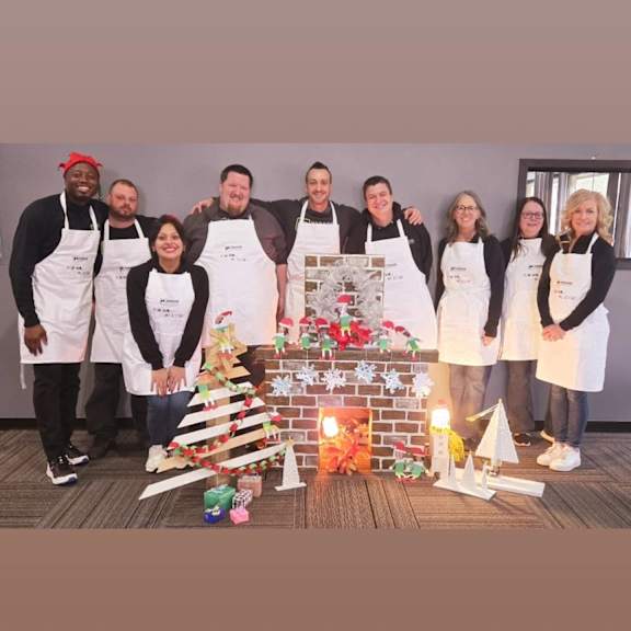 A group of people in aprons stand in front of a Christmas-themed display.