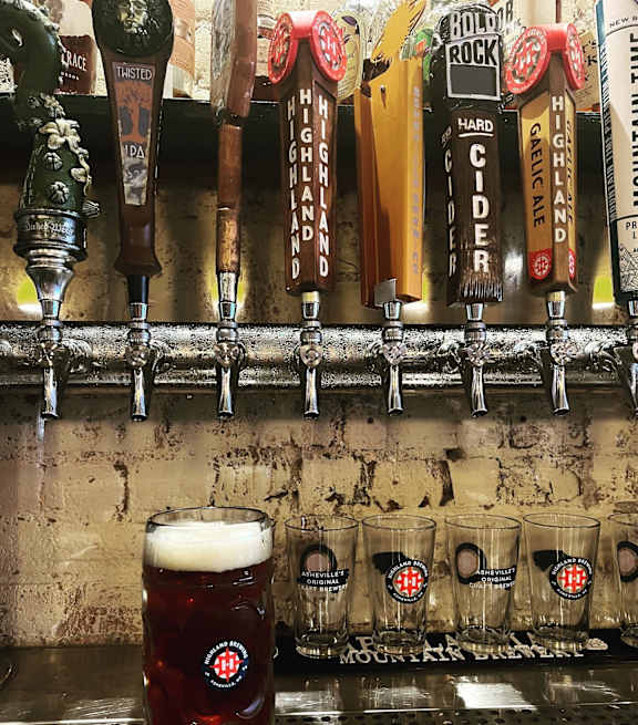 A glass of beer is in front of a row of beer taps.