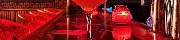 A cocktail is on a bar with a red lighting.