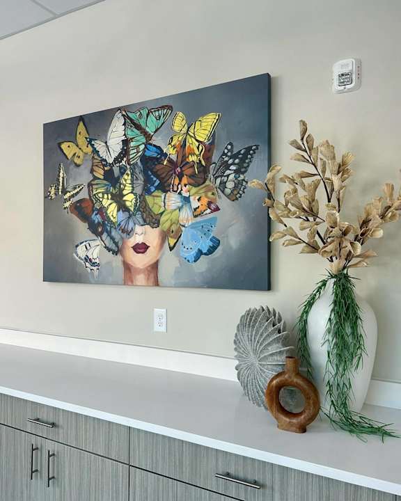 Painting of butterflies and flowers on a wall above a shelf with plants.