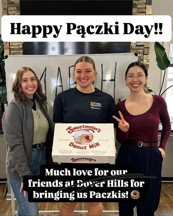Three people are standing in front of a sign, holding a box of Sweetwater's Donuts, celebrating Paczki Day.